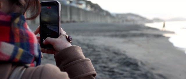 浜辺でスマートフォンを構える部員の手元